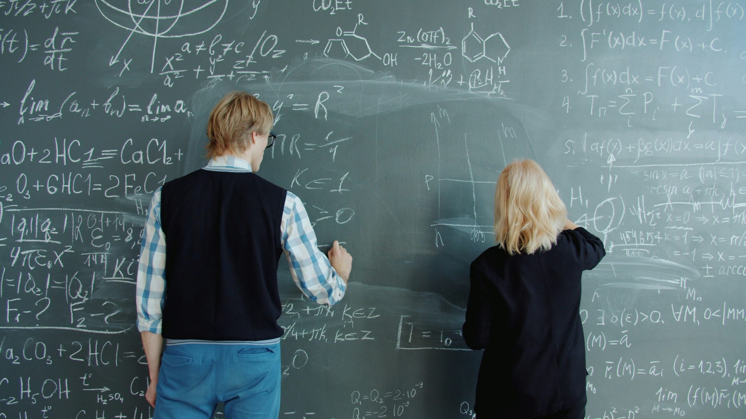 Humanoid robot and scientist collaborating on whiteboard equations - Man and woman are writing formulas on chalkboard working at science project together concentrated on education. Knowledge, people and school concept.